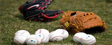 MLB gloves and baseballs with MLB logo against a grass background